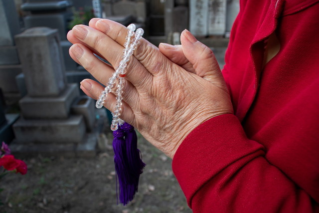 墓地で数珠を持つ高齢女性